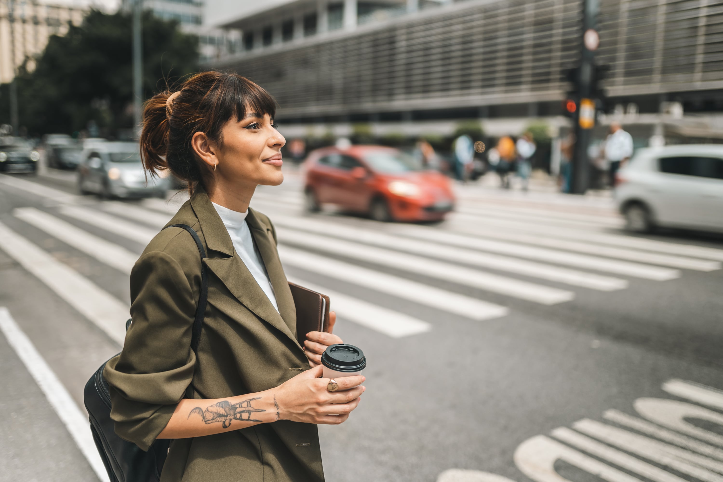 A woman crossing the street with a coffee, considering Brazil EOR services.
