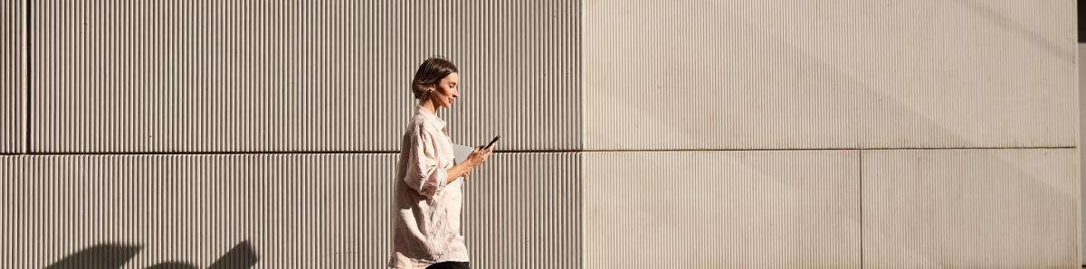 Confident businesswoman walking on street while looking at phone during sunset.
