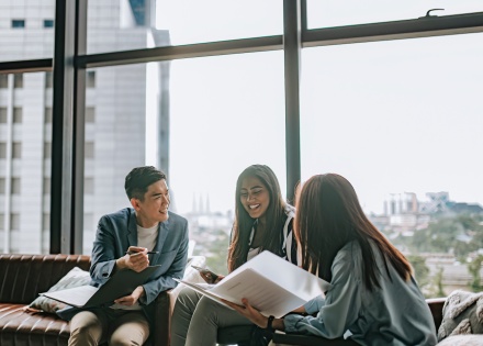 Three people sitting along a window and chatting