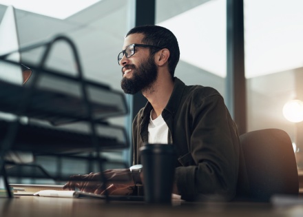 A happy male 1099 employee sitting at a desk and working on his laptop
