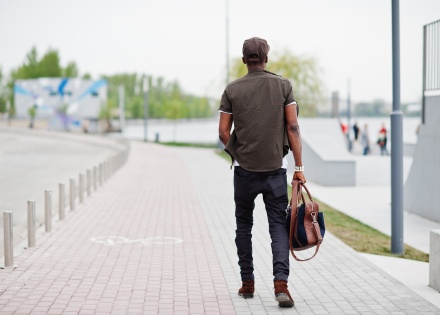 Back view of man holding backpack & walking along brick path