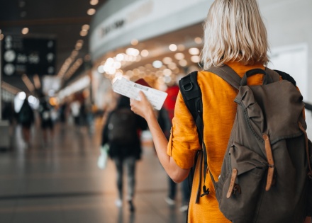 Person with a backpack walking through an airport holding a boarding pass.