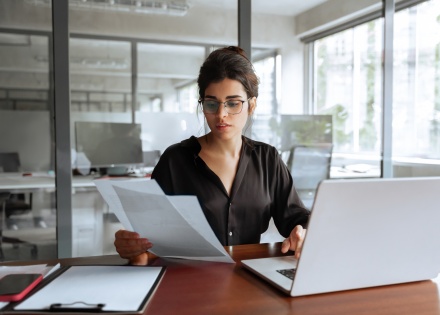 Businesswoman holding documents while working on her laptop on payroll taxes in Gabon