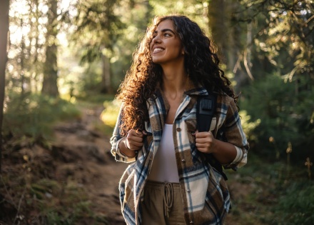 Cheerful woman with a backpack hiking on a forest path