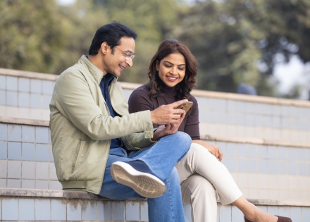A couple using a phone while spending leisure time in a park in India