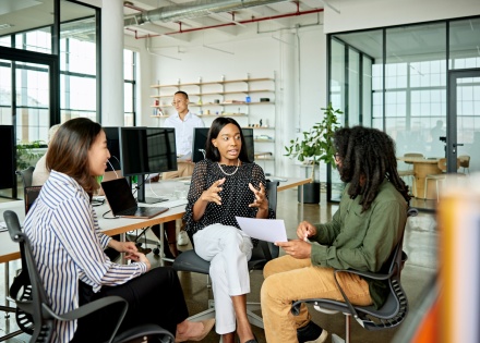 Three colleagues sitting in chairs discussing workplace culture in Qatar