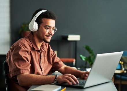 Young smiling man with headphones on typing on laptop