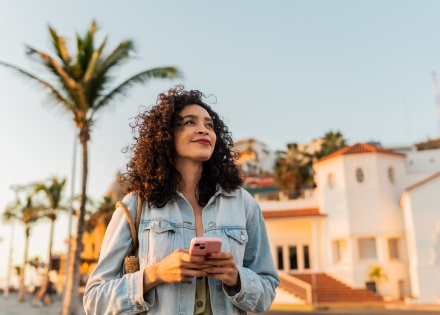 Young woman looking away, holding a mobile phone outdoors