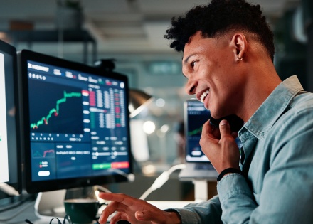 Male financial analysts working on two computer monitors