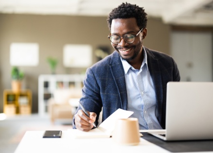 Male legal assistant writing in a notebook while working in office