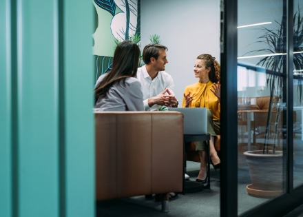 Three colleagues in a discussion at an office meeting room, representing an HR outsourcing team collaboration