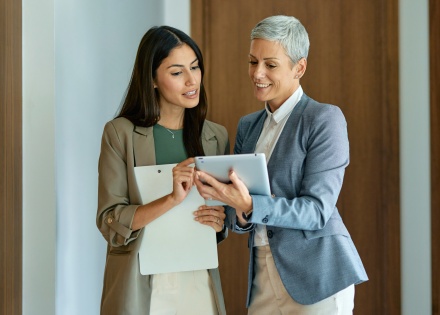 Two colleagues reviewing HR audit findings on a tablet in an office hallway