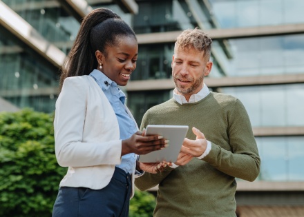 Two colleagues reviewing a tablet outside an office, using compensation management software.