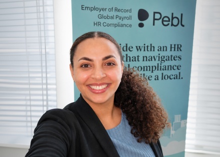 Solange Obawole, a Black woman with warm brown skin and naturally curly hair pulled into a ponytail, smiling at the camera in a blue top and business jacket, with a Pebl banner in the background. 