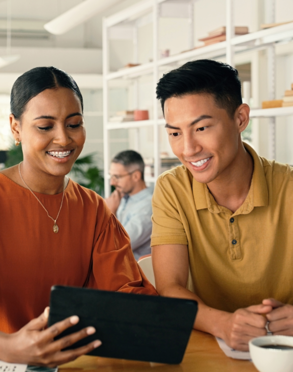 Man and woman at a coffee shop smiling, while looking at an iPad