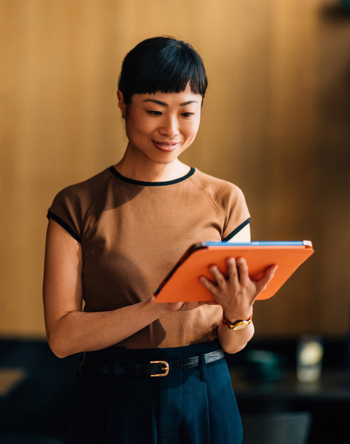 Professional woman walking and looking at EOR services on tablet.