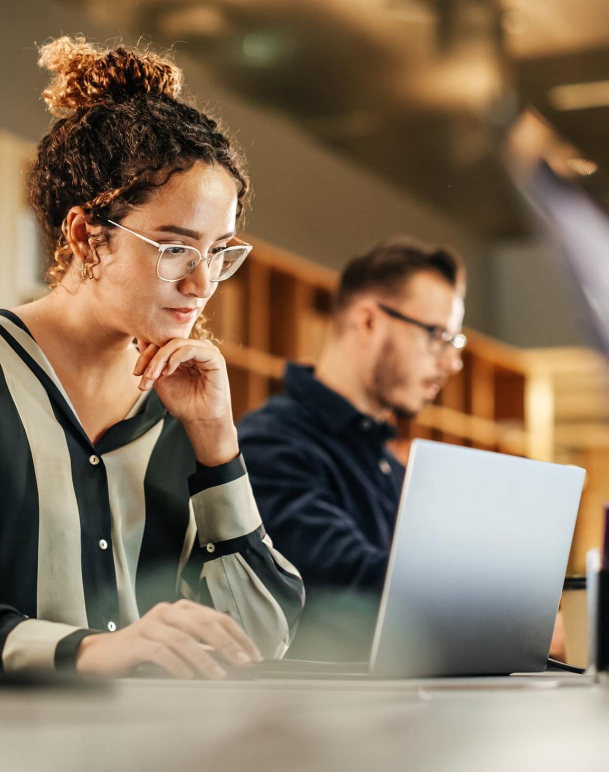 Colleagues sitting side-by-side on desk working on individual laptops.