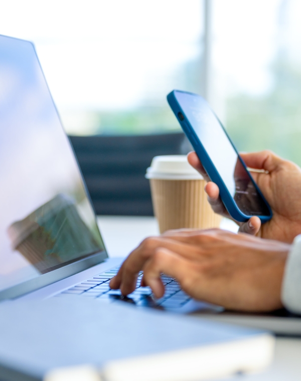 Zoomed-in image of laptop with hand on keyboard and other hand holding cell phone.