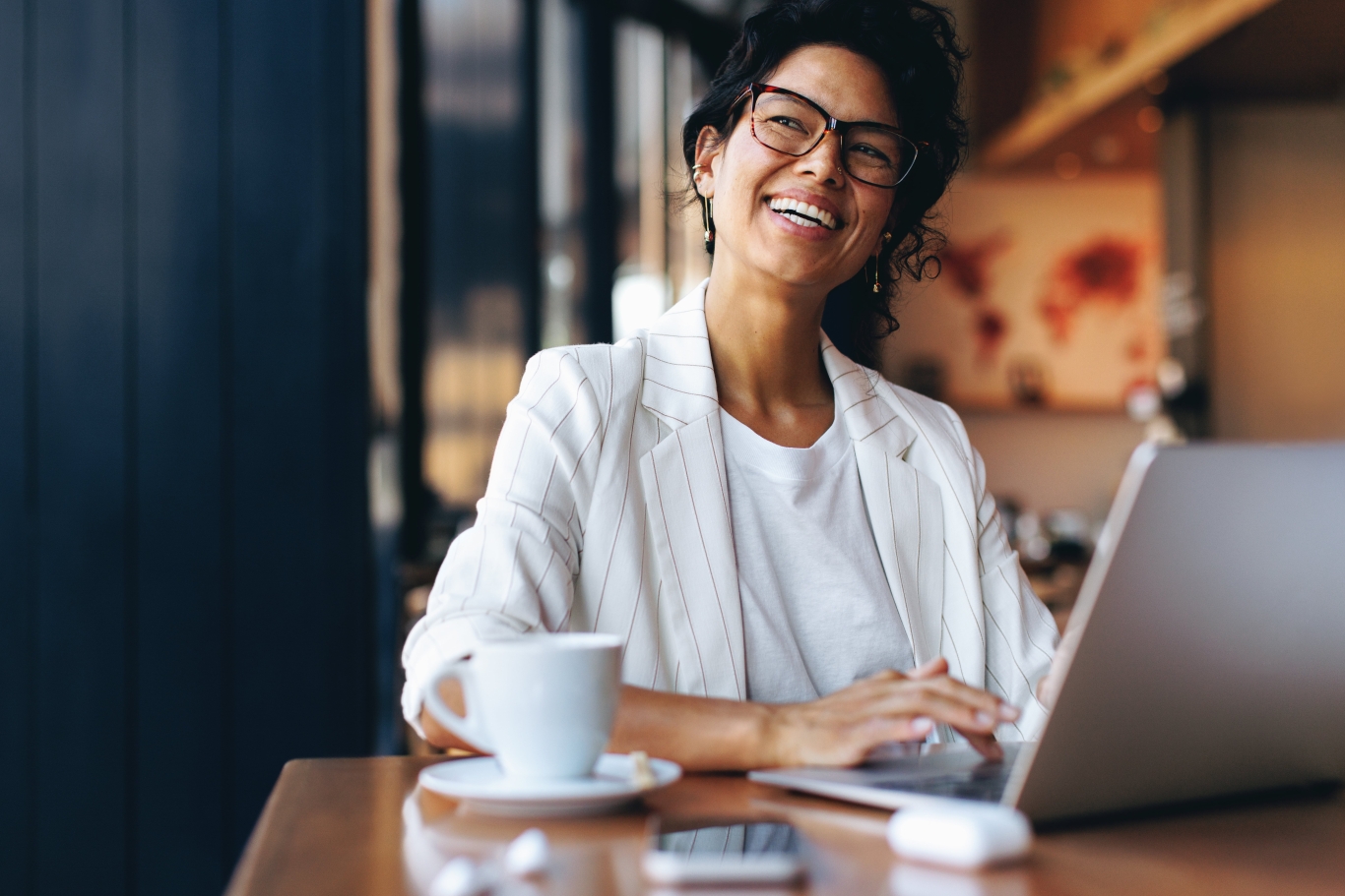 Smiling employer in white pinstripe suit sitting in cafe with laptop and coffee.
