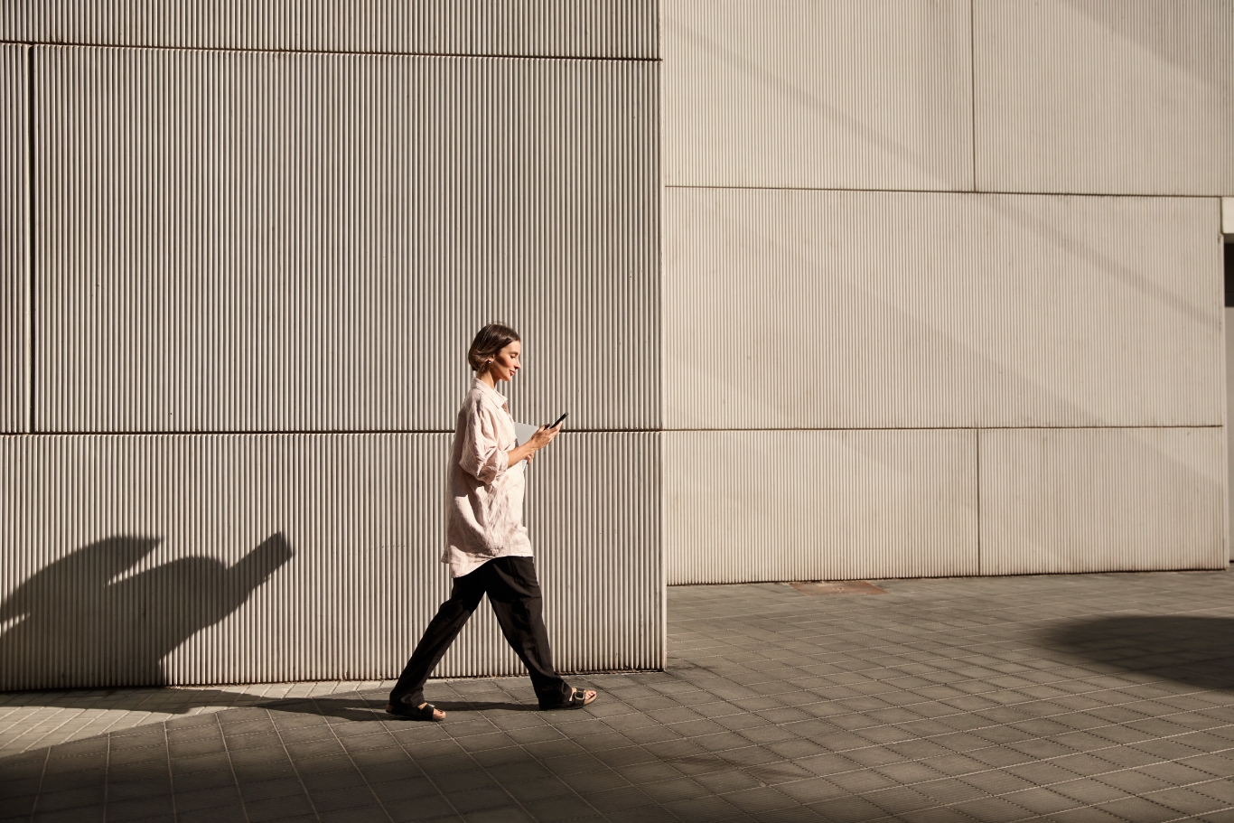 Confident businesswoman walking on street while looking at phone during sunset.
