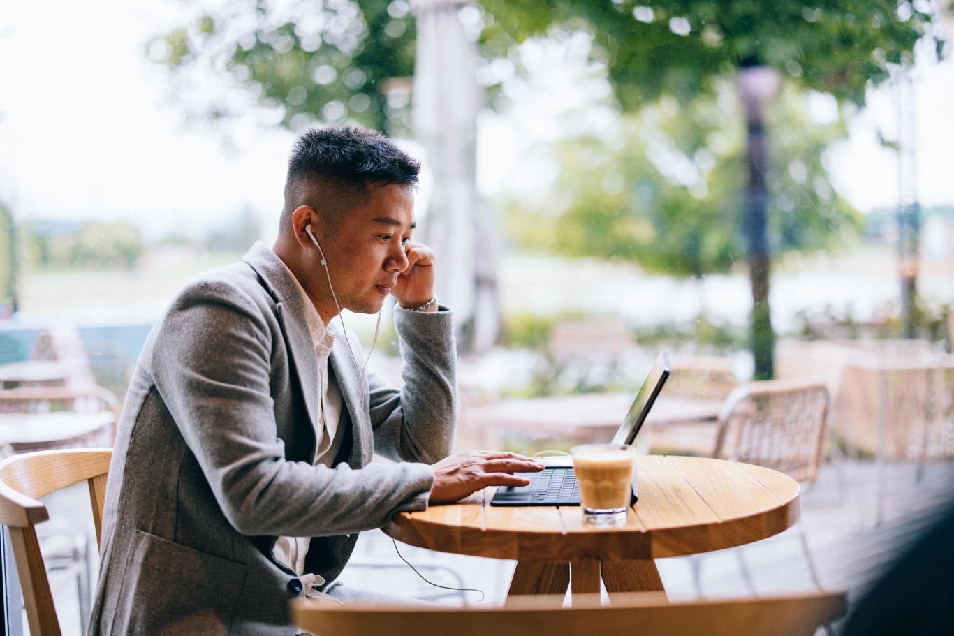 Professional legal team employee reviewing Pebl EOR services on laptop outdoors with headphones in and coffee.