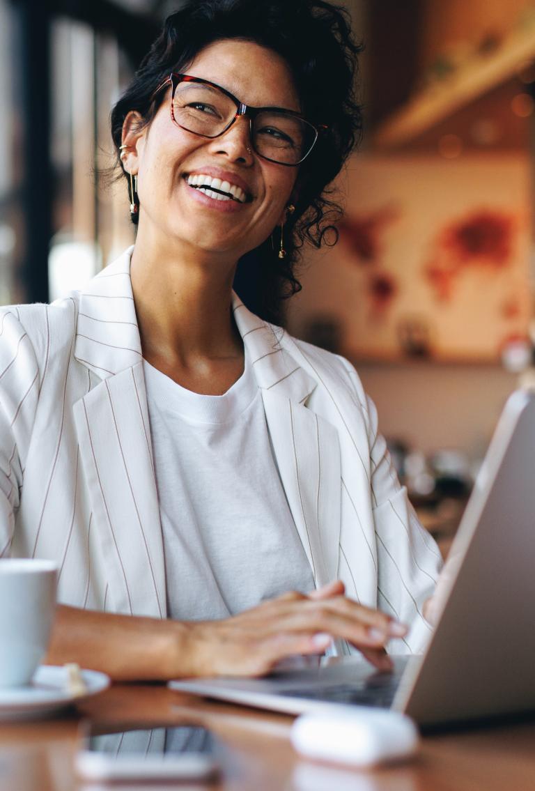 Smiling employer in white pinstripe suit sitting in cafe with laptop and coffee.