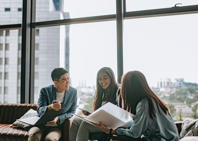 Three people sitting along a window and chatting