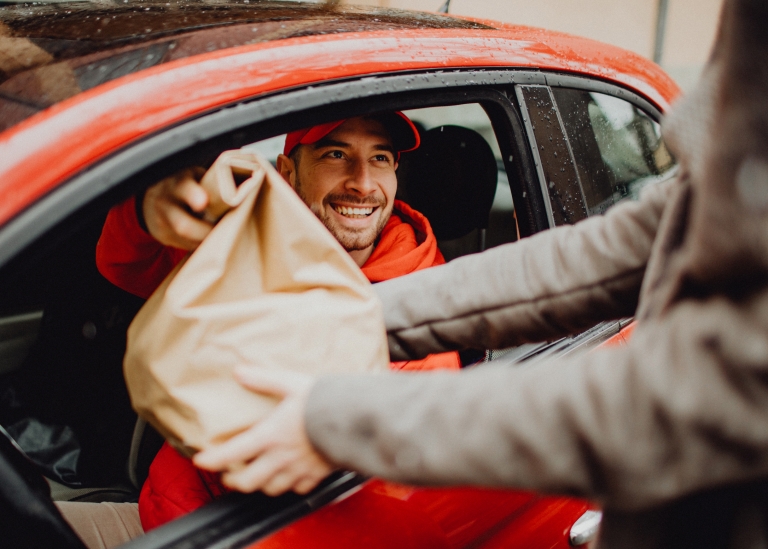 Delivery driver in red car hand customer food in brown paper bag