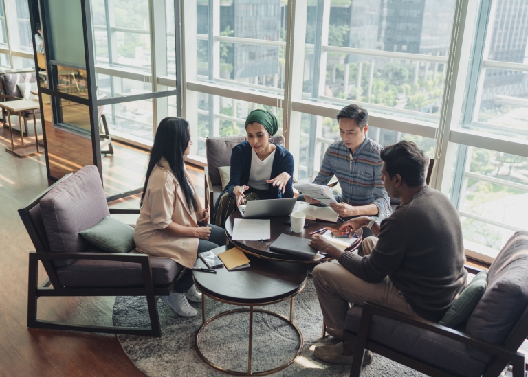 Four co-workers gather around a coffee table and discuss a project.