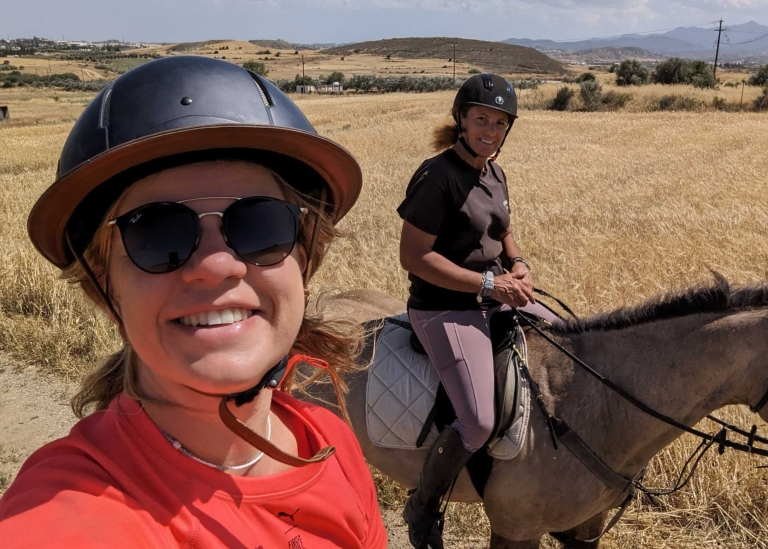 Pebl’s Janna Papageorghiou riding a horse with a friend while wearing a helmet and sunglasses