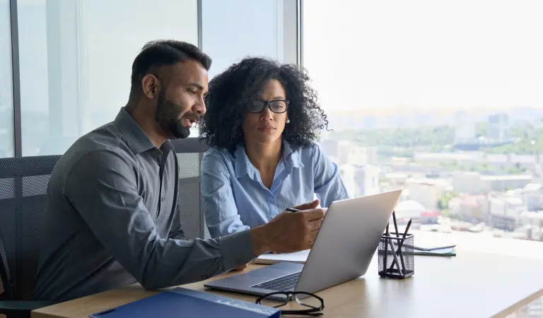 colleagues-sitting-at-desk-looking-at-laptop-computer-in-office.jpg