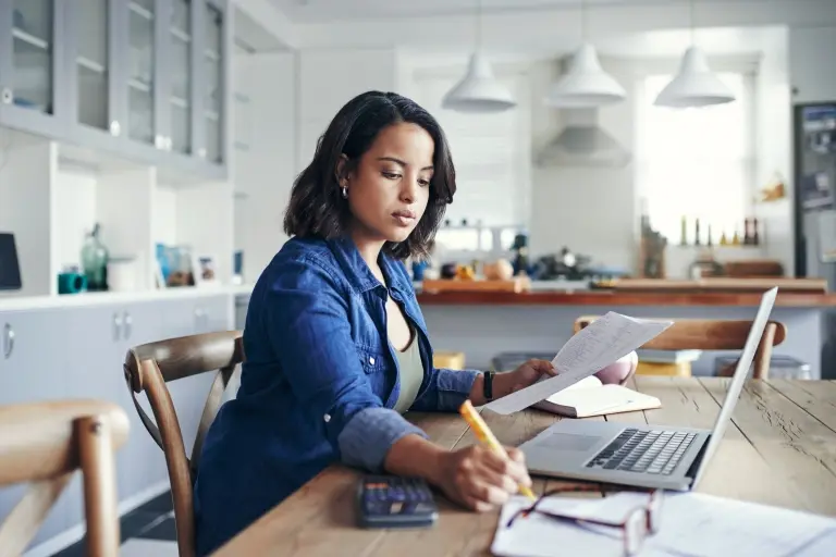 young-woman-using-a-laptop-and-going-through-paperwork-while-working-from-home.jpg