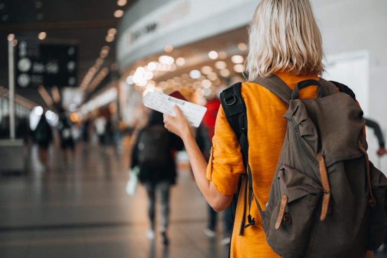 Person with a backpack walking through an airport holding a boarding pass.