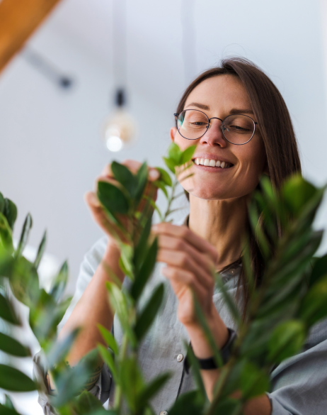 Woman with glasses smiles while tending to a plant
