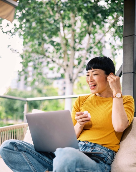 Female contractor sitting outside, putting airpod in her ear with laptop in lap.