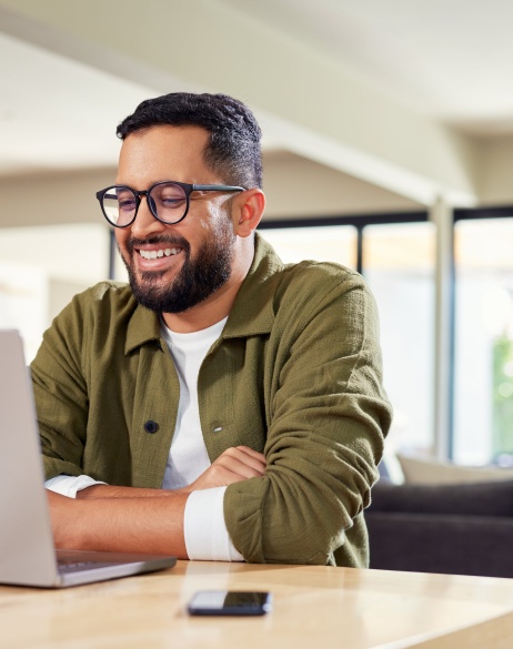 Male employer sitting in bright home setting looking at laptop of hiring global talent with Pebl.