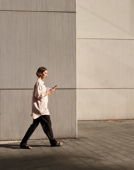 Confident businesswoman walking on street while looking at phone during sunset.