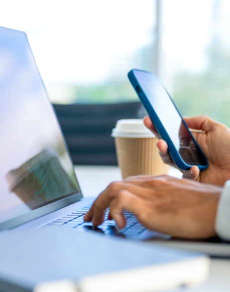 Zoomed-in image of laptop with hand on keyboard and other hand holding cell phone.