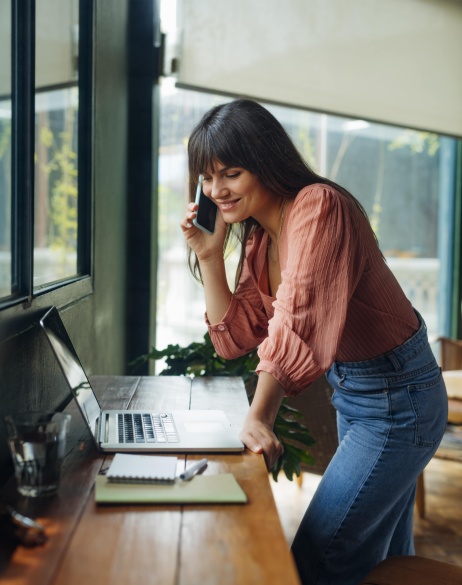 Female employer on cell phone discussing contractor conversion while looking at laptop.