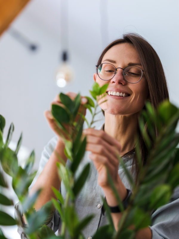 Woman with glasses smiles while tending to a plant