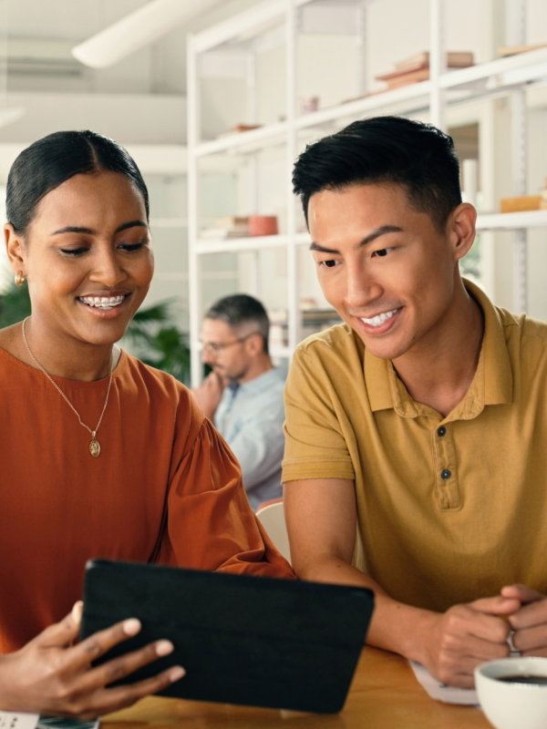 Man and woman at a coffee shop smiling, while looking at an iPad