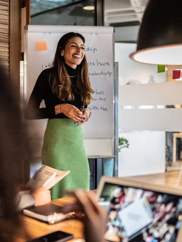 Woman hosting a working session at the front of a meeting room.