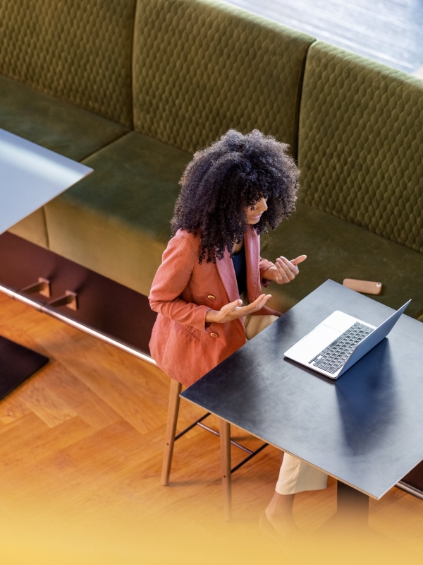 Overhead view of woman on laptop meeting, sitting at table in open space.