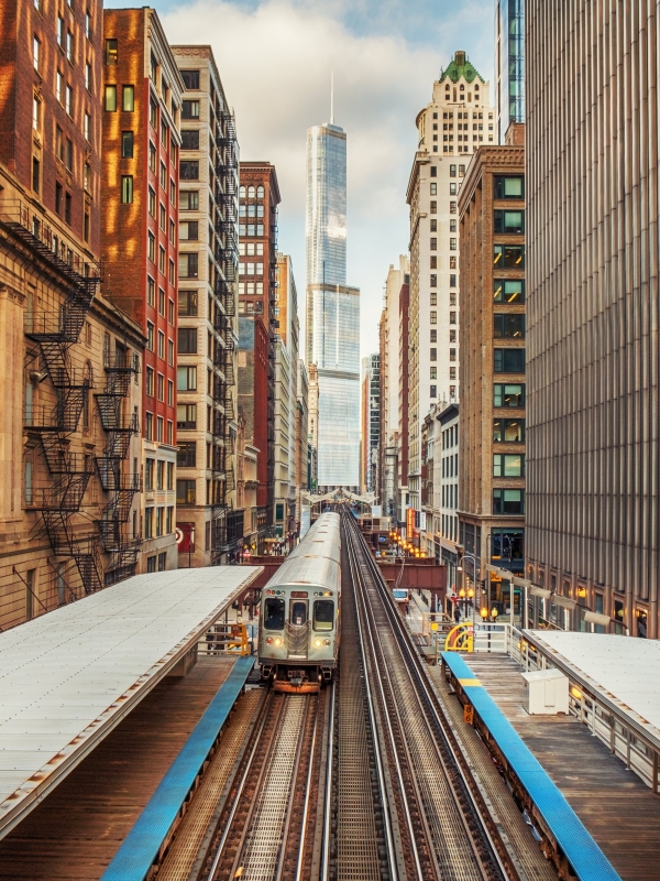 Chicago railway between high rises with metro approaching and cityscape in the background.
