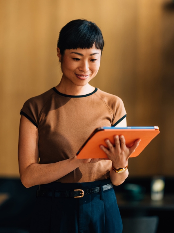 Professional woman walking and looking at EOR services on tablet.