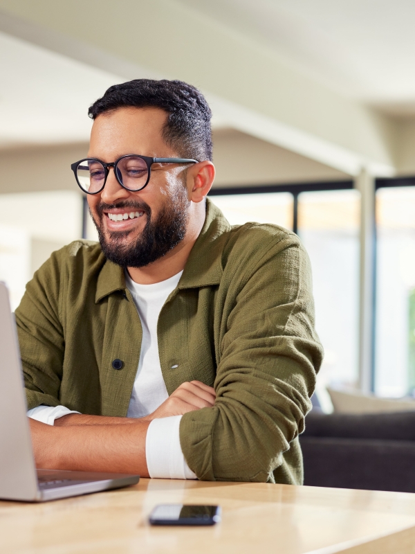 Male employer sitting in bright home setting looking at laptop of hiring global talent with Pebl.