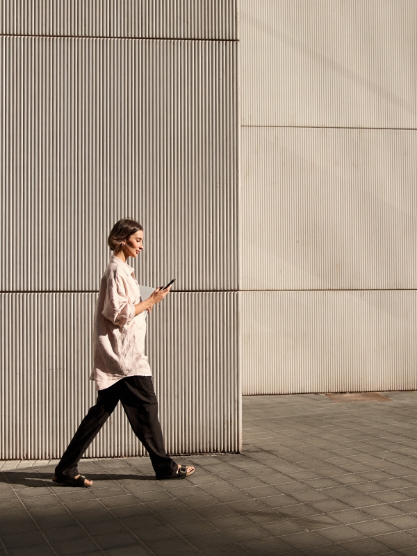 Confident businesswoman walking on street while looking at phone during sunset.