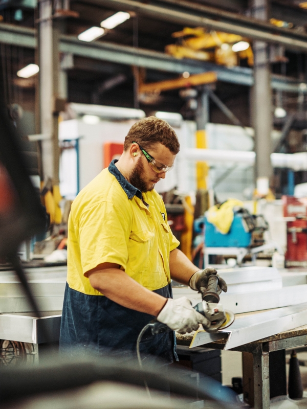 Man working with tool in manufacturing plant wearing gloves and safety glasses.
