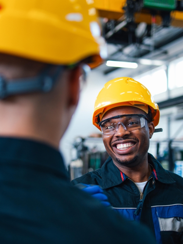 Three male colleagues wearing construction hats and safety glasses indoors.
