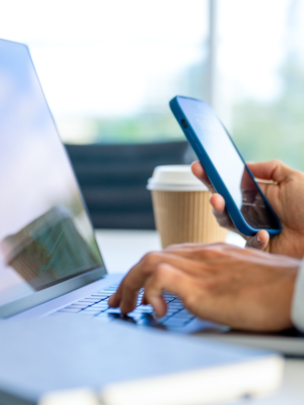 Zoomed-in image of laptop with hand on keyboard and other hand holding cell phone.